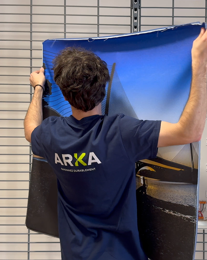 Technicien ARKA installant une toile tendue sur un cadre lumineux
